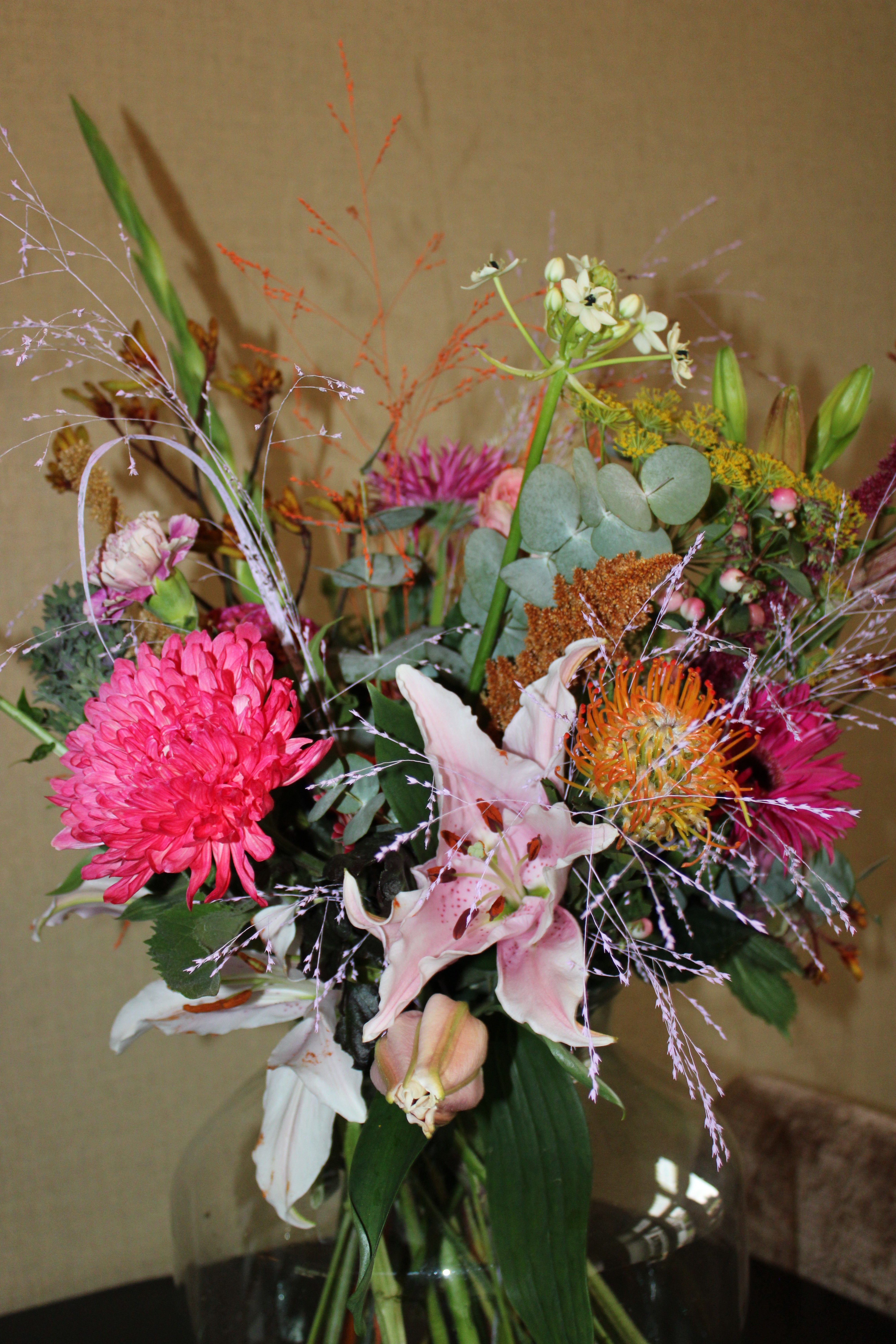 Groot verrassingsboeket met kleurrijke seizoensbloemen, waaronder chrysanten, lelies en eucalyptus, handgebonden in een glazen vaas – Boeketje van Drosje.
